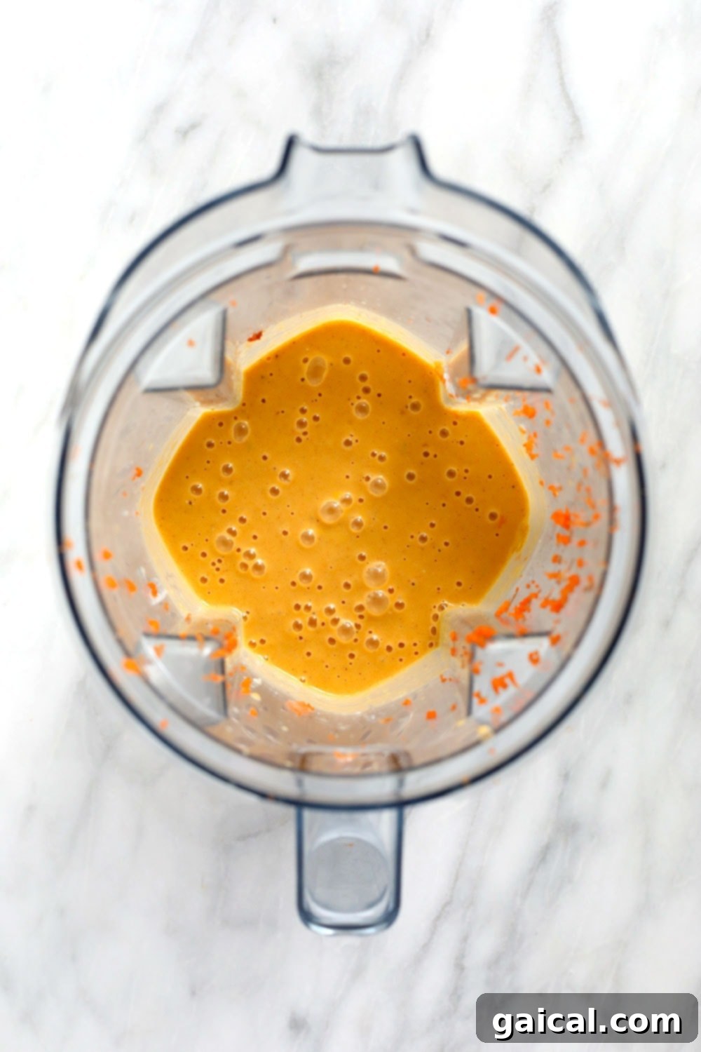 A vibrant carrot cake smoothie swirling inside a high-speed Vitamix blender, demonstrating its smooth, uniform, and frothy consistency during the blending process.