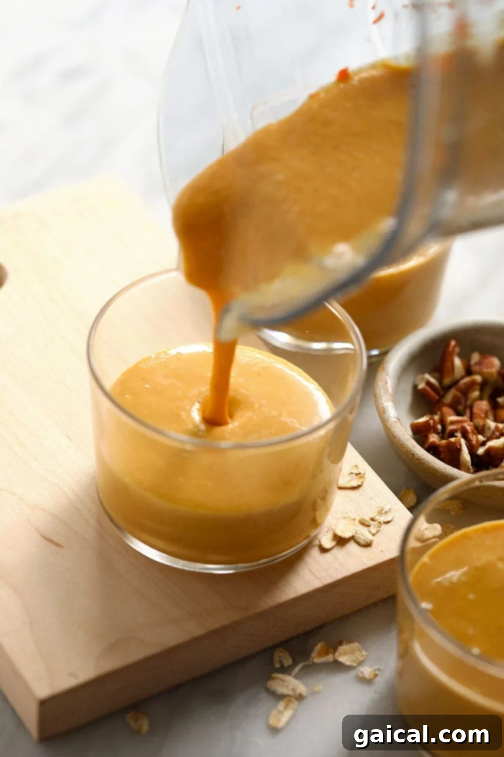 The smooth, creamy texture of a freshly blended carrot cake smoothie being gracefully poured from a blender into a clear tall glass, creating a visually appealing stream.