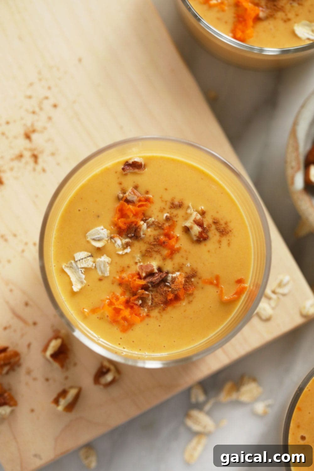 A beautifully presented glass of creamy carrot cake smoothie, generously topped with crunchy walnuts, rolled oats, and delicate shredded carrot for an irresistible finish.