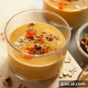 A bowl of creamy carrot cake smoothie, beautifully topped with a sprinkle of oats and a delicate drizzle of cashew butter, artfully arranged on a rustic wooden cutting board.
