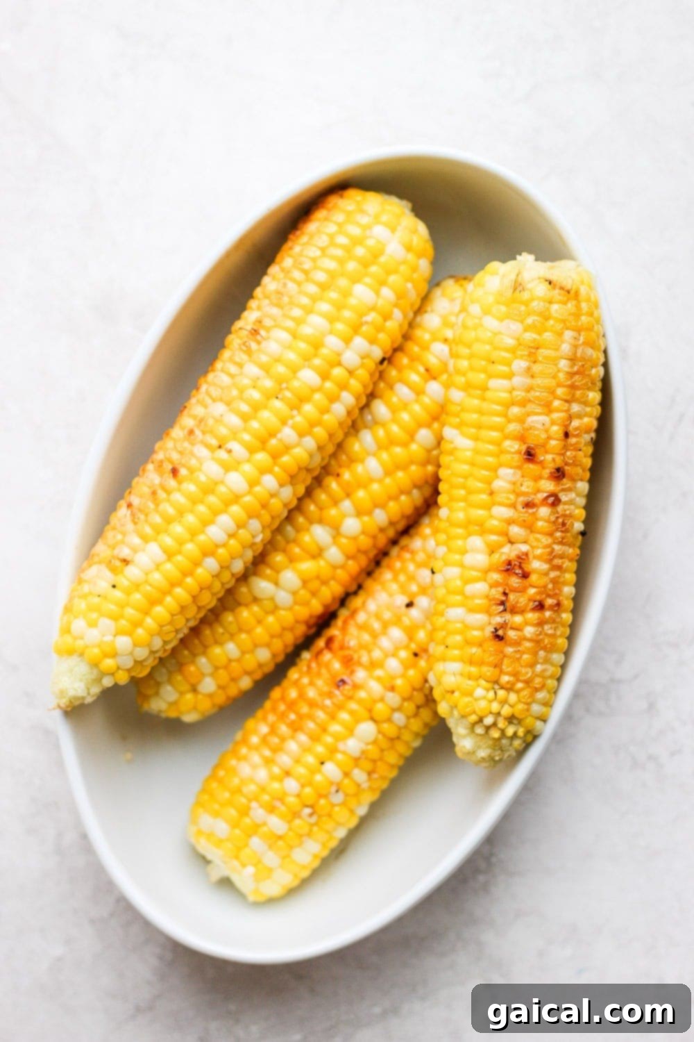 Foil Packet Grilled Corn 2 Perfectly grilled corn on the cob, still in its foil, resting on a serving platter with fresh herbs, ready to be devoured.