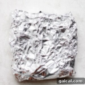 A tightly sealed foil packet containing an ear of corn, ready for grilling.