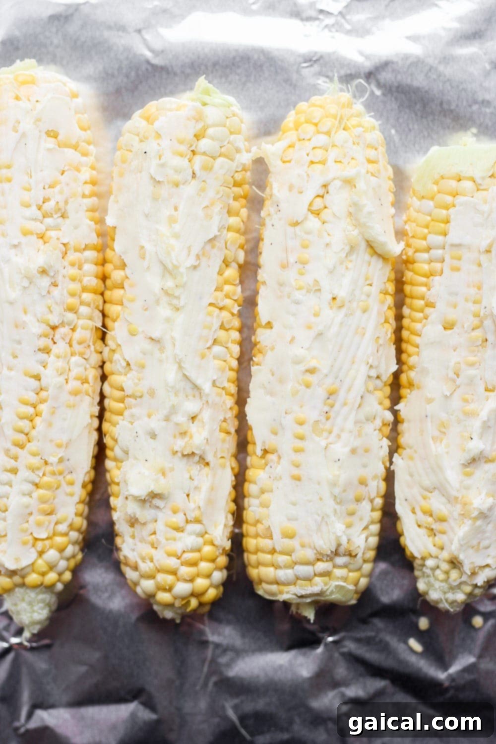 Foil Packet Grilled Corn 5 An ear of corn generously coated with butter and seasonings, placed on a sheet of aluminum foil, perfectly prepared for wrapping and grilling.