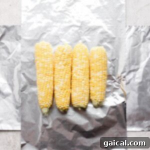 Four ears of corn laid out on aluminum foil, preparing for wrapping.