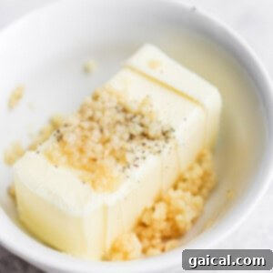 A small white bowl containing a mixture of softened butter, minced garlic, salt, and pepper.