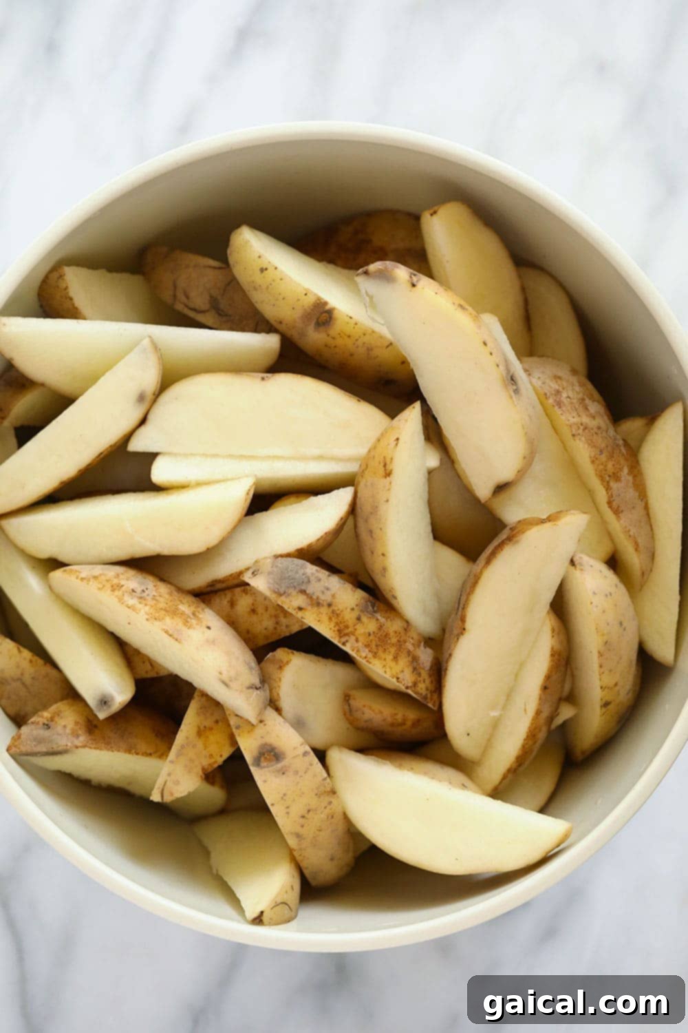Crispy Roasted Potato Wedges 3 Freshly chopped russet potato wedges in a stainless steel bowl, ready for seasoning.