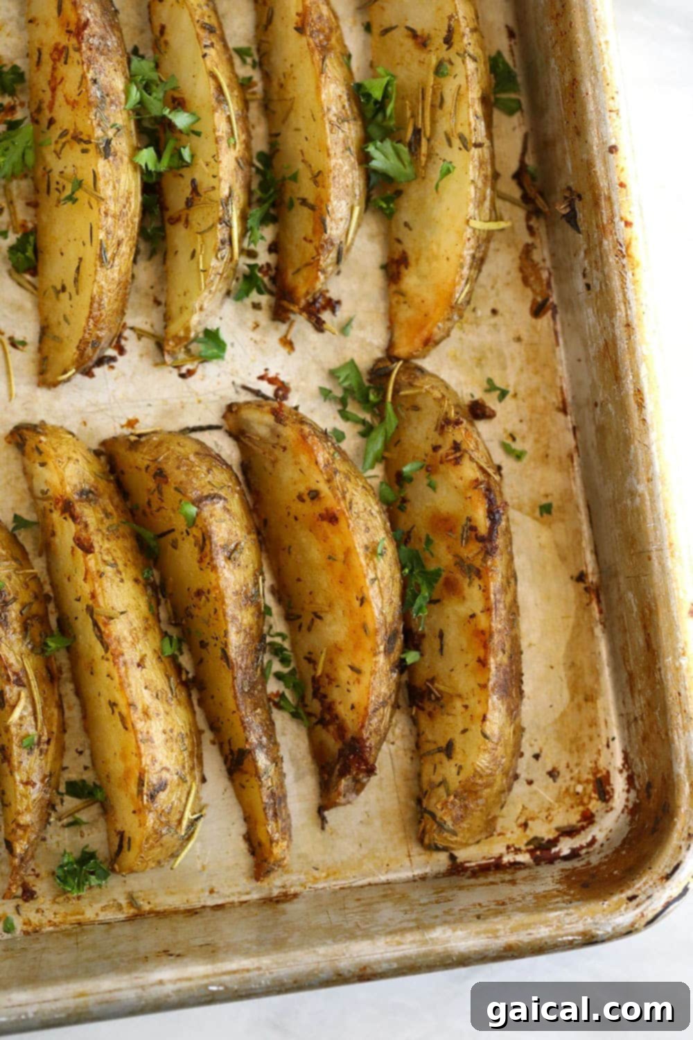 Crispy Roasted Potato Wedges 6 Golden brown potato wedges on a baking sheet, freshly baked and sprinkled with green parsley.