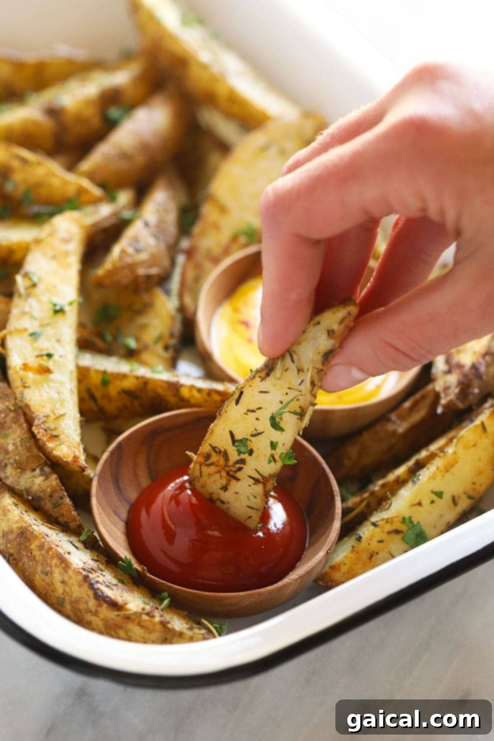 Crispy Roasted Potato Wedges 9 A crispy oven-baked potato wedge being dipped into a bowl of vibrant red ketchup.