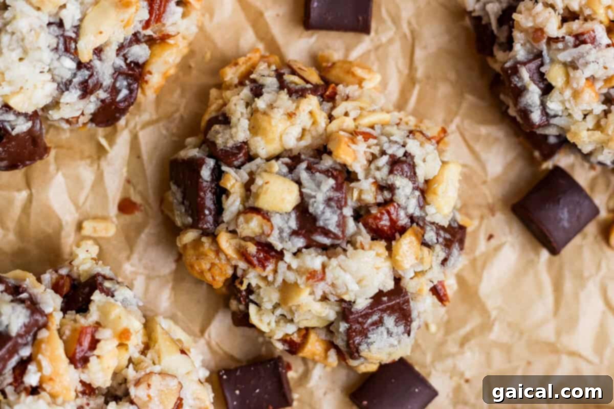 A close-up of clusters of cookies with visible nuts, oats, and large chocolate chunks on crumpled brown parchment paper.