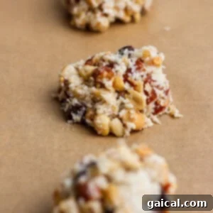 Three unbaked clusters of mixed nuts, dried fruit, and shredded coconut on a sheet of brown parchment paper.