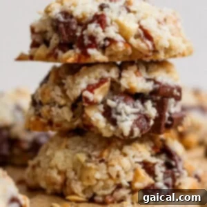 Three coconut, nut, and chocolate chunk cookies are stacked on top of each other on a piece of parchment paper.