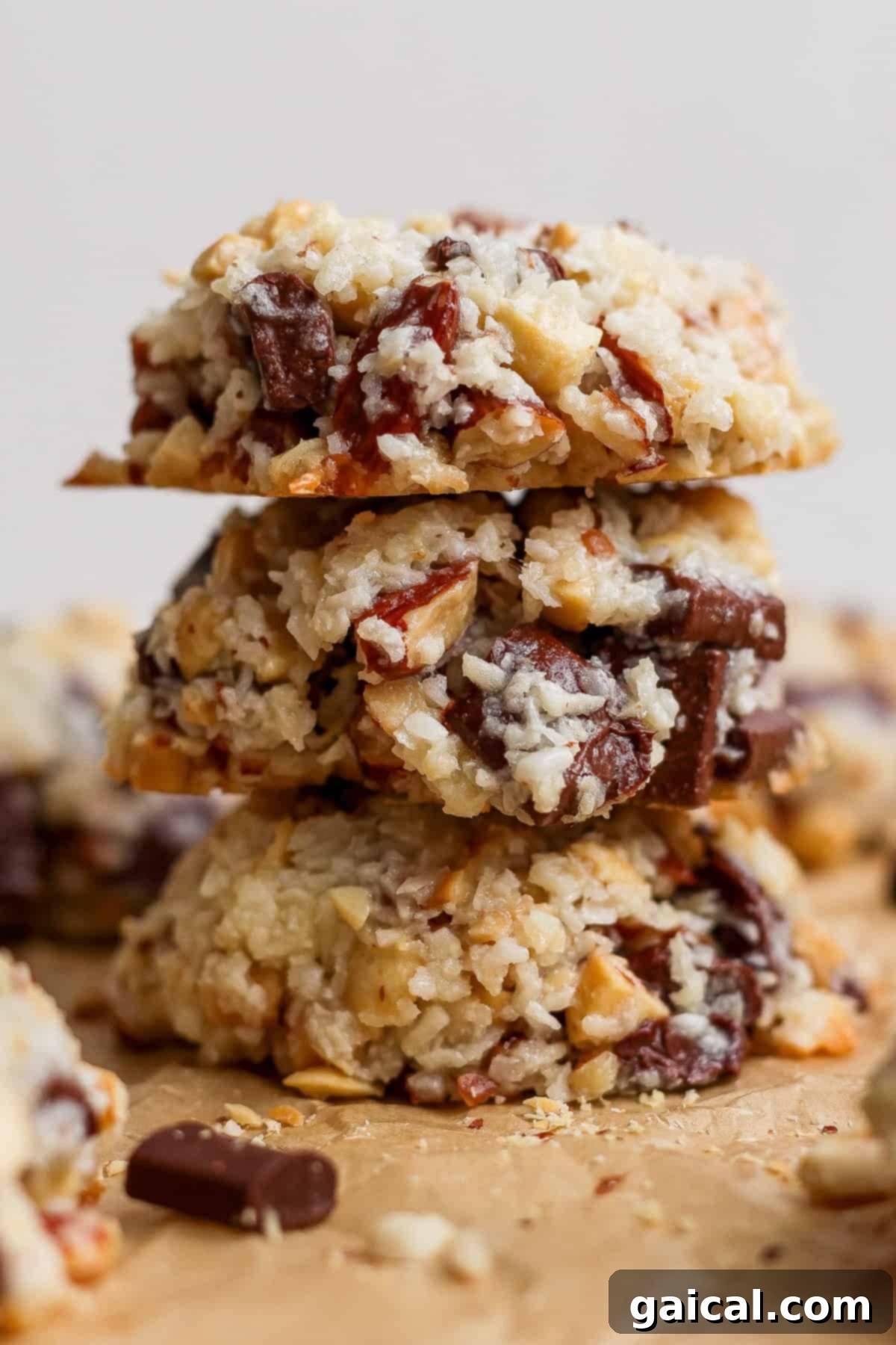 Three coconut, nut, and chocolate chunk cookies are stacked on top of each other on a piece of parchment paper.