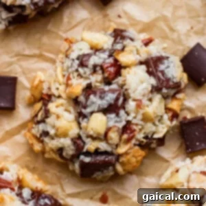 A close-up of a homemade cookie with visible chunks of chocolate, nuts, and oats, resting on a piece of crumpled parchment paper.