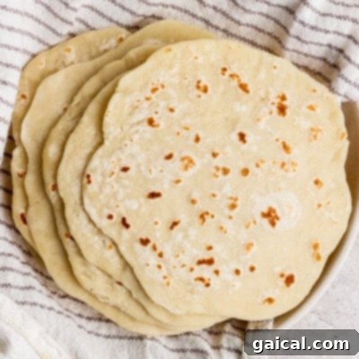 A stack of homemade flour tortillas rests on a striped kitchen towel.