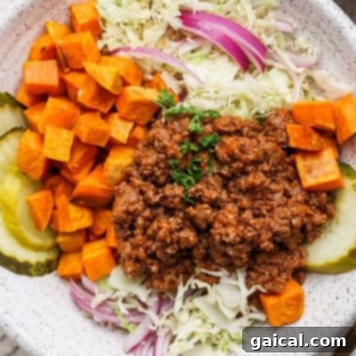 A plate with ground beef, diced sweet potatoes, shredded cabbage, red onions, and pickle slices.