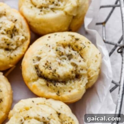 Close-up of savory pastry rolls topped with shredded cheese and herbs, arranged in a metal basket lined with white parchment paper.