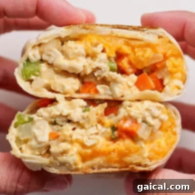 Two hands hold a halved breakfast burrito filled with scrambled eggs, cheese, onions, green peppers, and orange bell peppers.