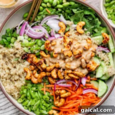 A bowl of salad with quinoa, edamame, onions, cucumbers, carrots, cashews, and green onions, topped with a creamy dressing.