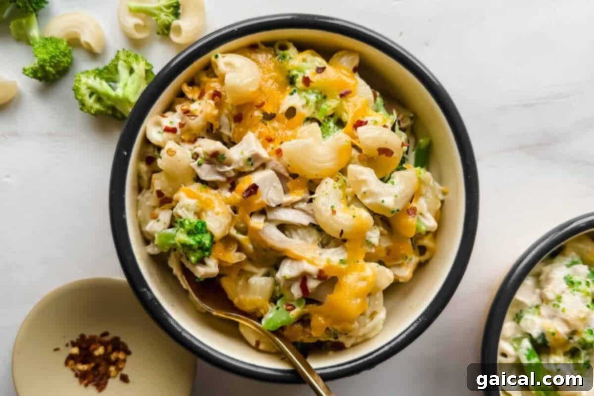 A mouthwatering bowl of Chicken Broccoli Cottage Cheese Mac and Cheese, topped with melted cheese and a sprinkle of red pepper flakes, with a spoon enticingly placed in the bowl.