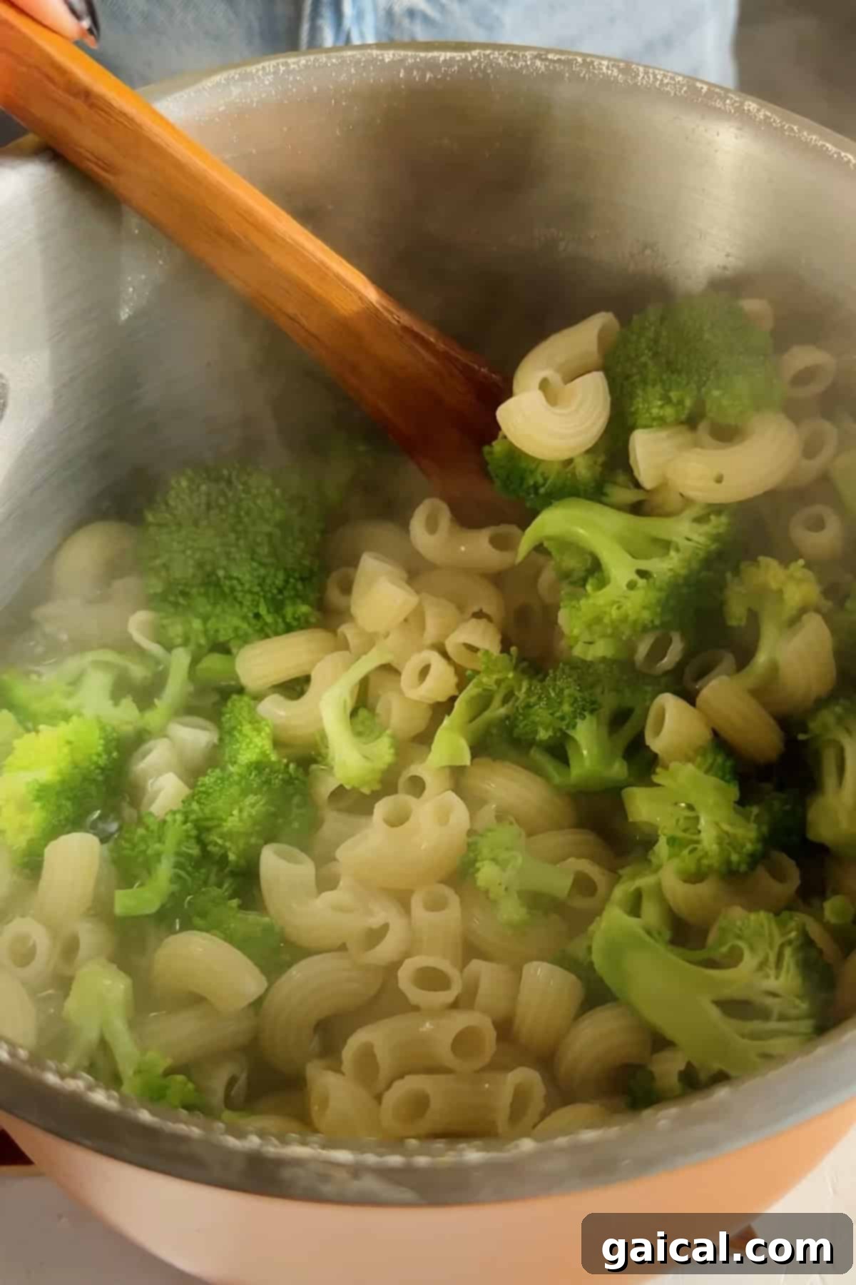 A pot filled with perfectly cooked pasta and vibrant green broccoli, being gently stirred with a wooden spoon, with steam rising to indicate its freshness.