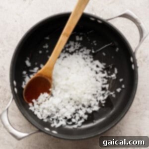 Chopped onions in a black pot being stirred with a wooden spoon on a light-colored surface.