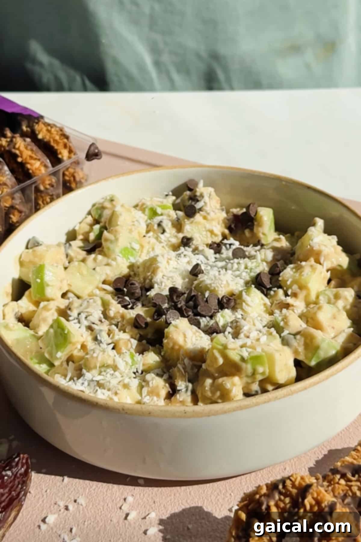 A refreshing bowl of Caramel deLites Apple Salad with diced apples, shredded coconut, and chocolate chips, surrounded by granola bars and cookies.
