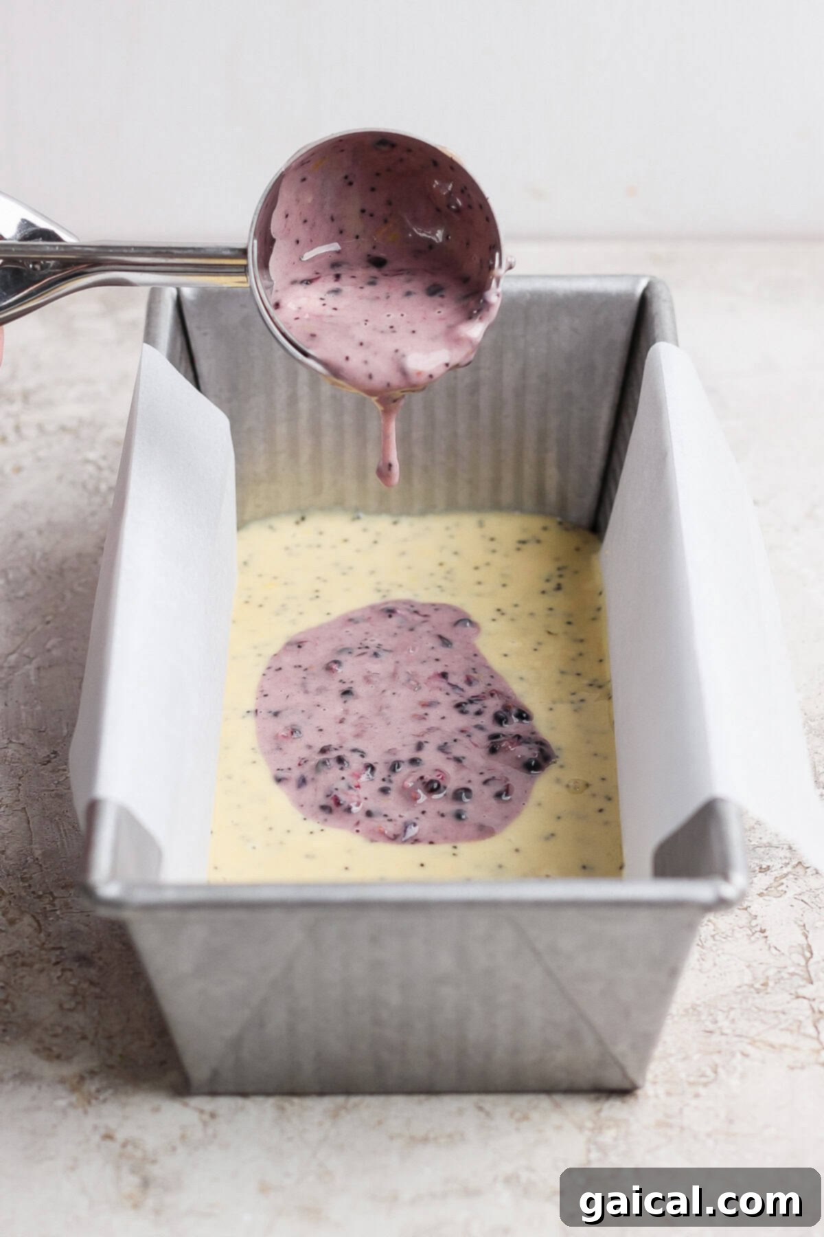 Pouring the blackberry batter over the lemon poppy seed batter in a loaf pan.