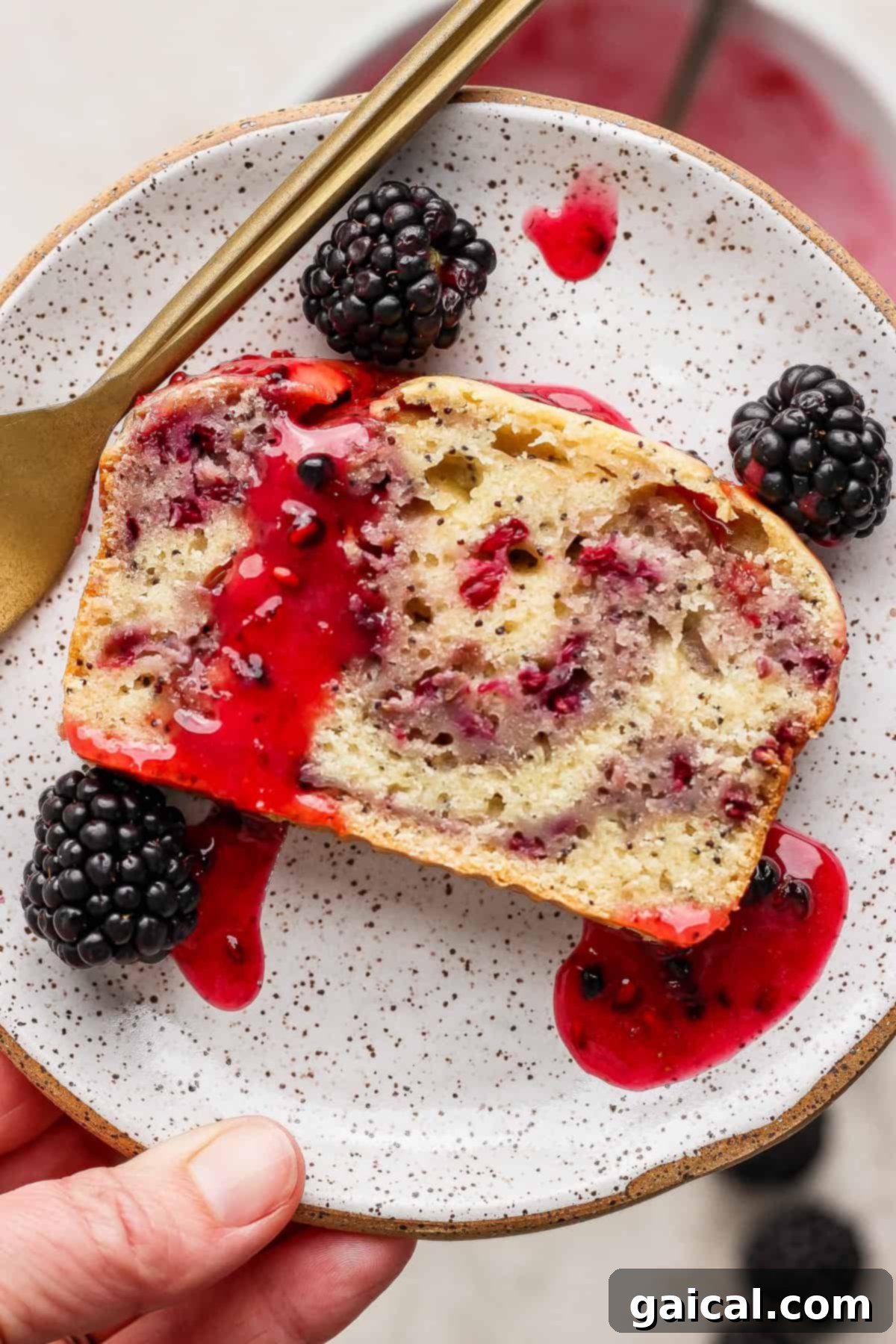 A slice of blackberry lemon poppy seed loaf with blackberry glaze and fresh blackberries.
