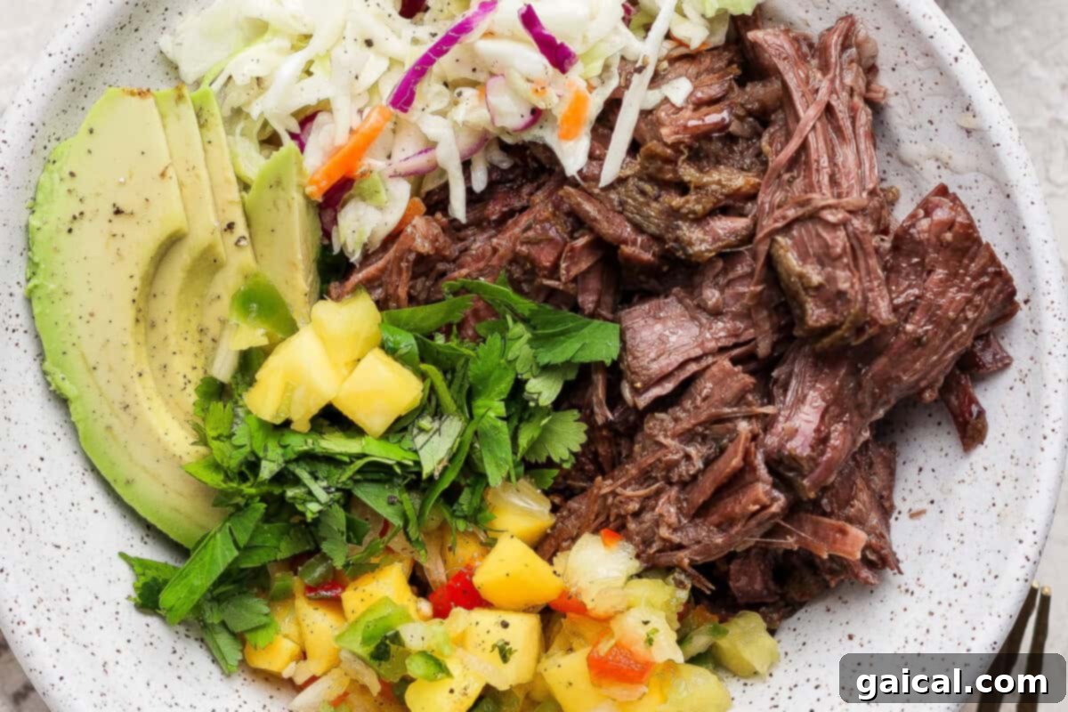 A delicious bowl of slow cooker shredded beef with avocado, coleslaw, cilantro, and pineapple salsa.