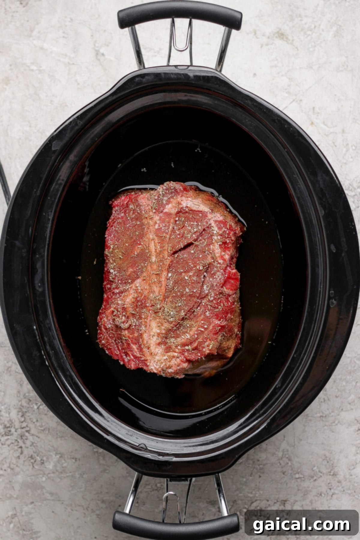 Seasoned chuck roast nestled in beef broth and Worcestershire sauce in a slow cooker.
