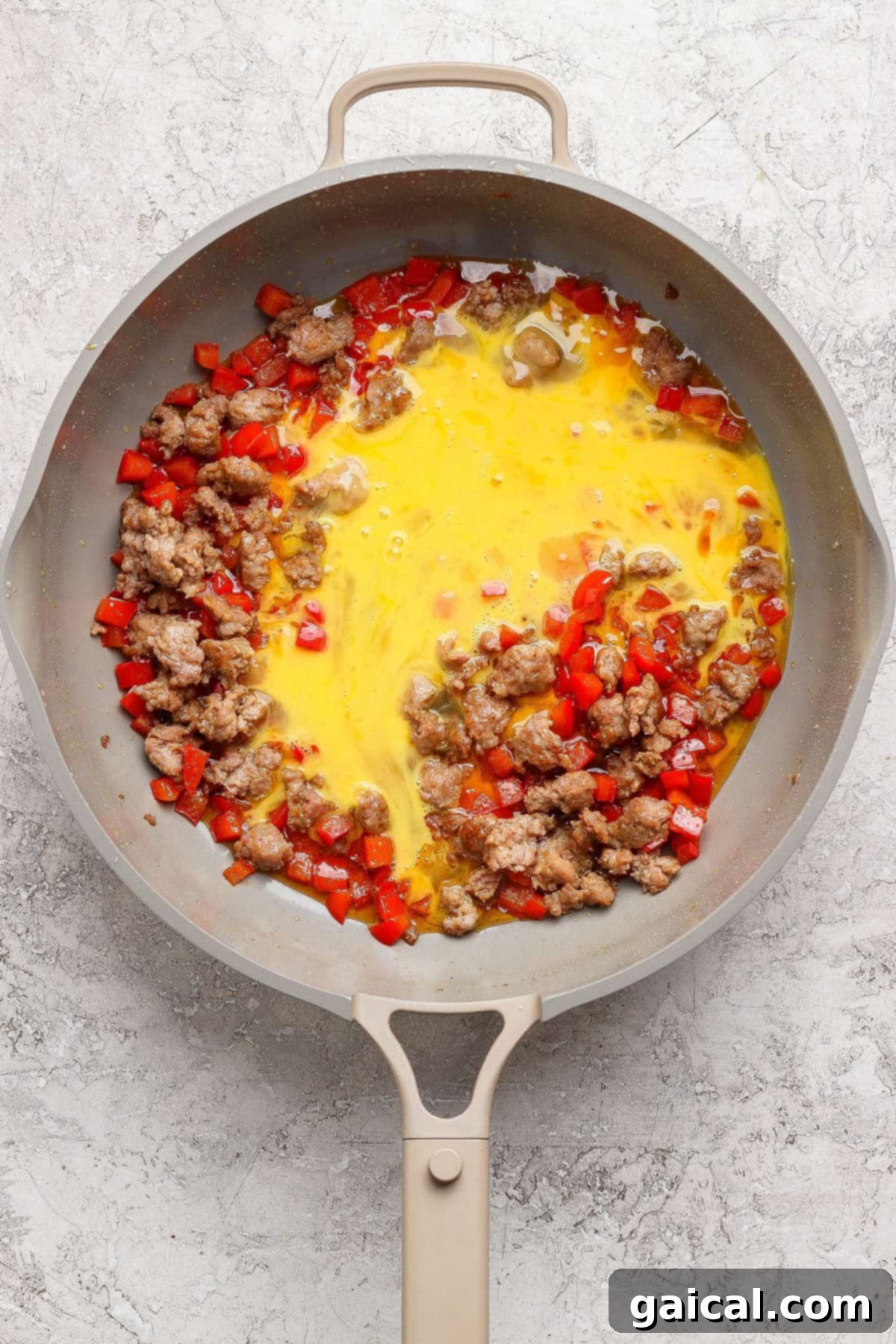 Scrambled eggs, sausage, and red bell peppers cooking in a skillet