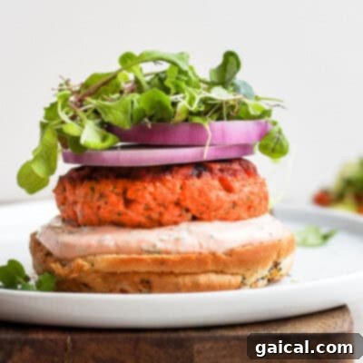 Delicious salmon burgers served with arugula and red onion on a white plate, showcasing their tender texture and vibrant flavors.