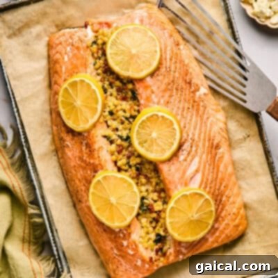 A beautifully stuffed salmon fillet, garnished with fresh herbs and lemon slices, resting on parchment paper on a baking tray.