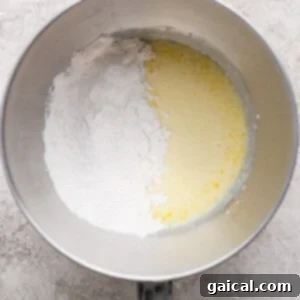 Protein Packed Cottage Cheese English Muffins 10 A metal mixing bowl containing flour on one side and a yellow liquid mixture on the other, placed on a light textured surface, showing the ingredients before mixing.