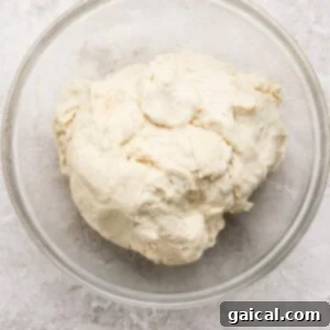 Protein Packed Cottage Cheese English Muffins 11 A clear glass bowl containing a ball of raw, unbaked dough sits on a light textured surface, covered for rising.