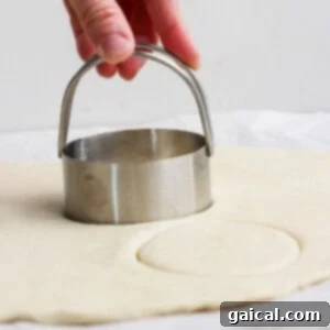 Protein Packed Cottage Cheese English Muffins 12 A hand presses a round metal biscuit cutter into rolled-out dough on a flat surface, demonstrating the shaping process.