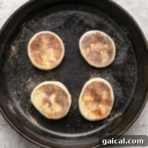 Protein Packed Cottage Cheese English Muffins 14 Four partially cooked English muffins in a cast iron skillet on a light textured surface, browning on the stovetop.