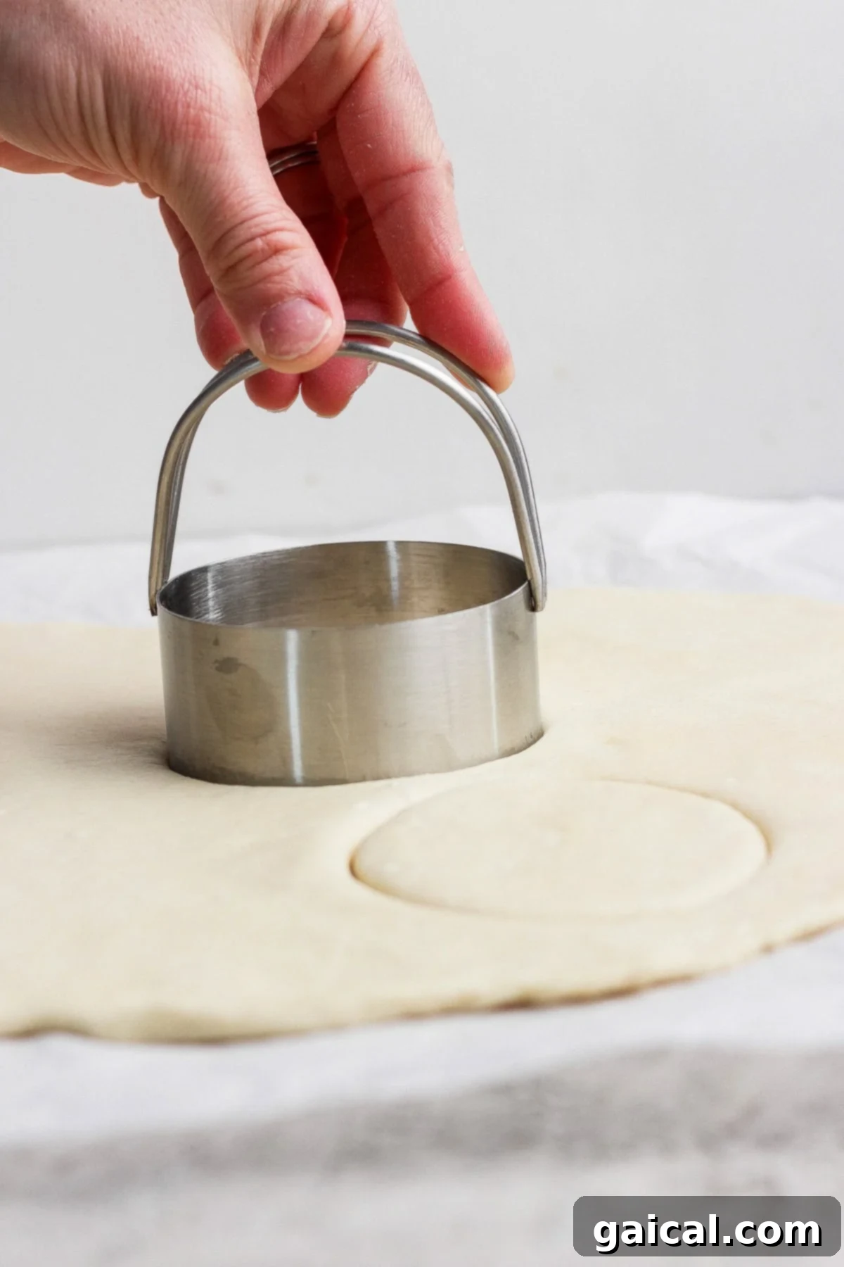 Protein Packed Cottage Cheese English Muffins 3 A hand presses a round metal biscuit cutter into rolled-out dough on a flat surface, demonstrating the shaping process for English muffins.