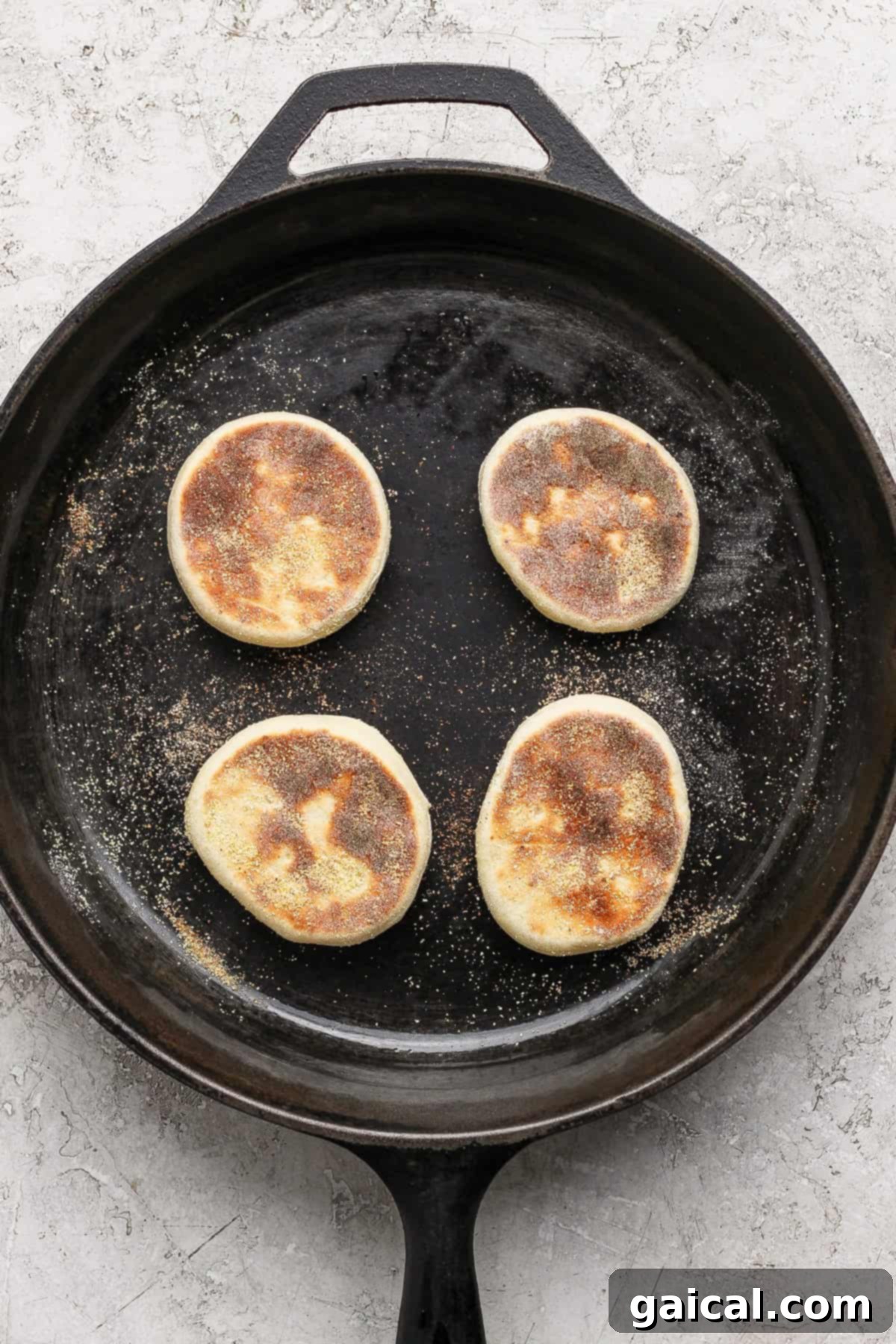 Protein Packed Cottage Cheese English Muffins 5 Four partially cooked English muffins gently sizzling in a cast iron skillet on a light textured surface, showing the browning process.