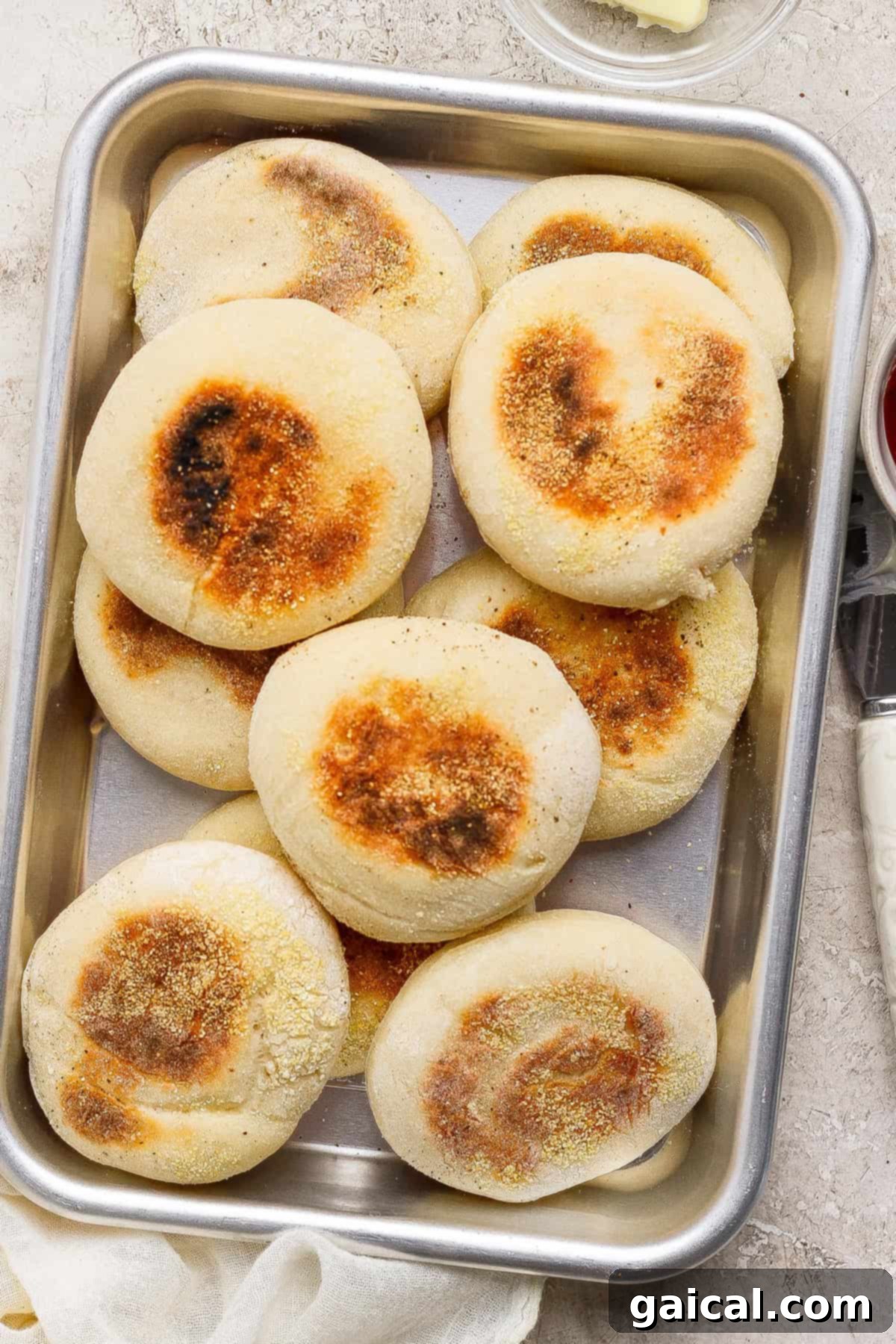 Protein Packed Cottage Cheese English Muffins 6 A metal tray filled with nine perfectly golden-brown homemade English muffins, each with a lightly toasted top and a delicate dusting of cornmeal, showcasing their finished appearance.