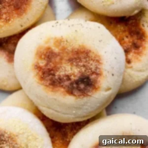 Protein Packed Cottage Cheese English Muffins 8 A close-up of several golden-brown English muffins topped with cornmeal, stacked together on a light surface, ready to be enjoyed.