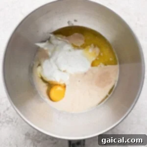 Protein Packed Cottage Cheese English Muffins 9 A mixing bowl containing yogurt, one egg, melted butter, and liquid yeast mixture on a light textured surface, ready for blending.