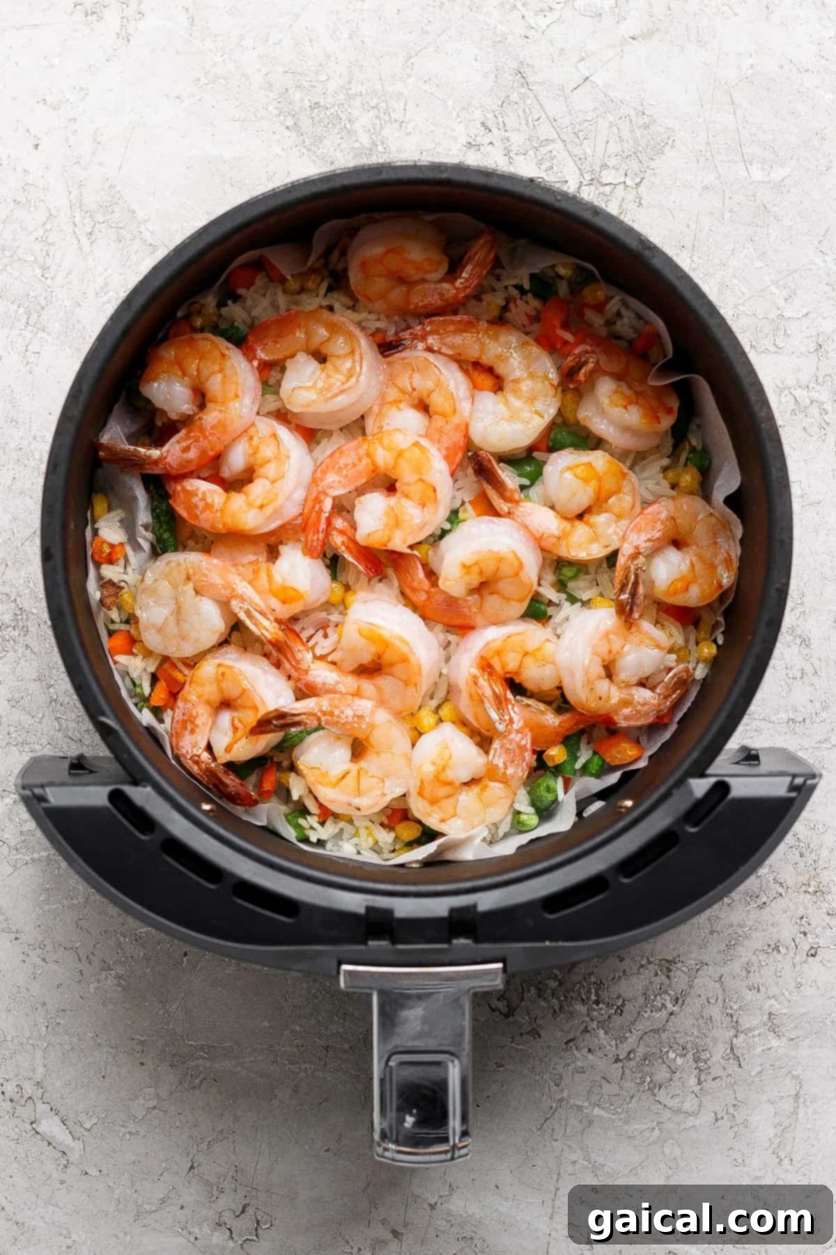A top-down view of the uncooked shrimp, rice, and vegetables spread in an even layer in the air fryer, ensuring even cooking.