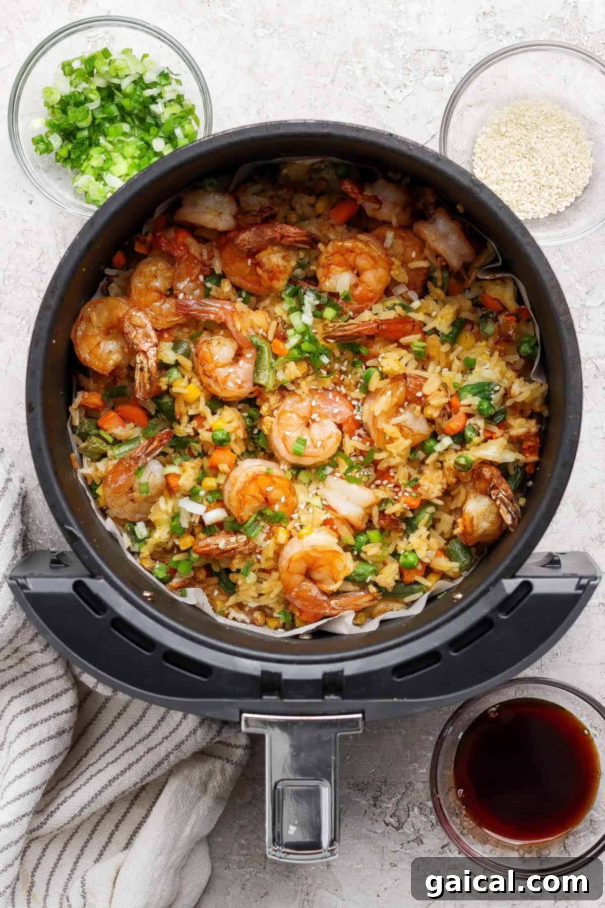 The fully cooked air fryer fried rice, tossed with shrimp, vegetables, and egg, is shown in the basket, garnished and ready to serve.