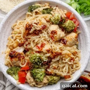 Bowl of ramen noodles with pieces of chicken, broccoli, red bell peppers, sesame seeds, and a chili oil sauce.