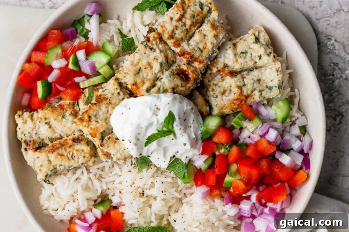 A bowl of white rice topped with grilled kebab pieces, diced red onion, red and green bell peppers, and a dollop of yogurt garnished with a mint leaf.