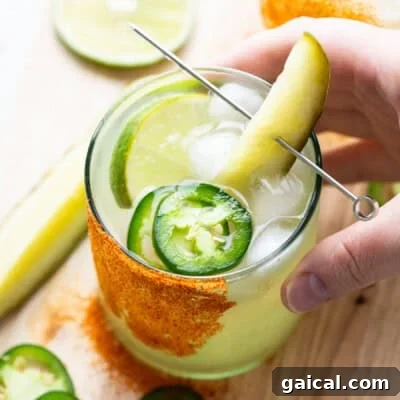A hand holding a glass of drink with a pickle and lime.