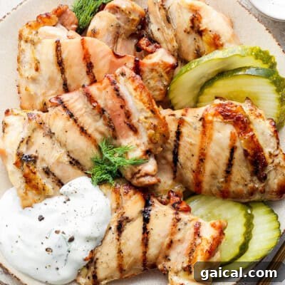 Grilled chicken breast slices served with pickles and a dollop of sour cream on a plate.