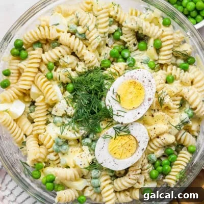 A bowl of fusilli pasta salad with green peas, chopped dill, and sliced hard-boiled egg halves on top.