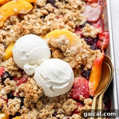 A dessert tray with fruit crisp topped with two scoops of vanilla ice cream and a spoon on the right side.